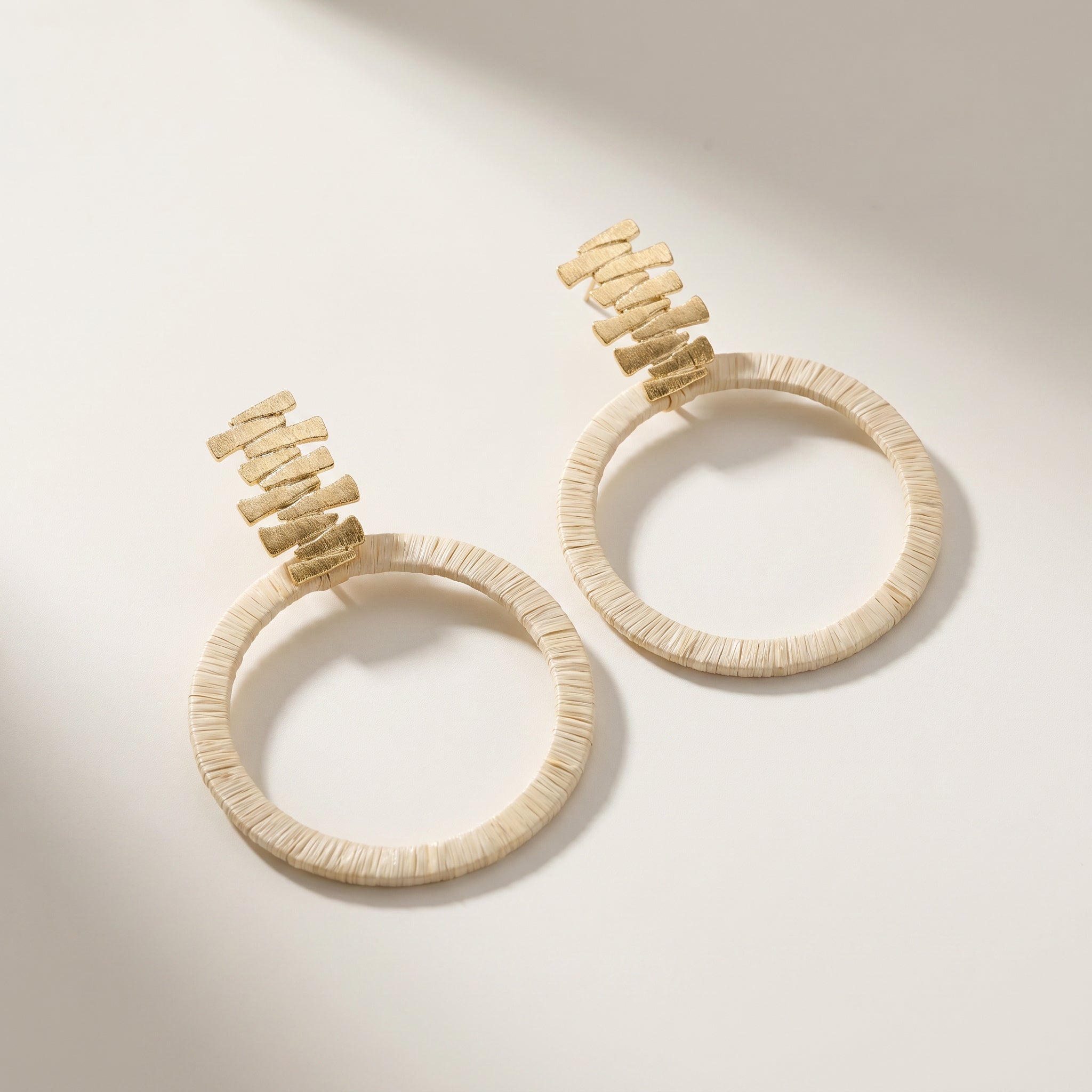 Pair of beige Purplee Store Buriti Sculptural Velune Earrings with gold accents on a light background