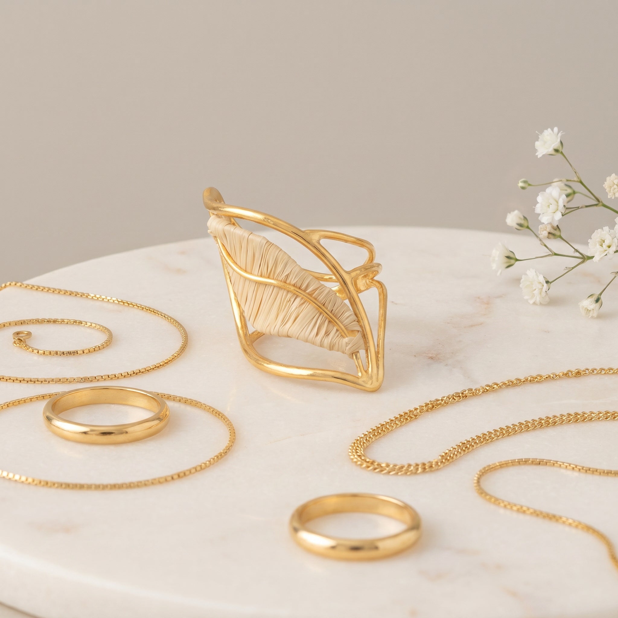 Gold jewelry including rings and a necklace on a marble surface with small white flowers. Purplee Store
