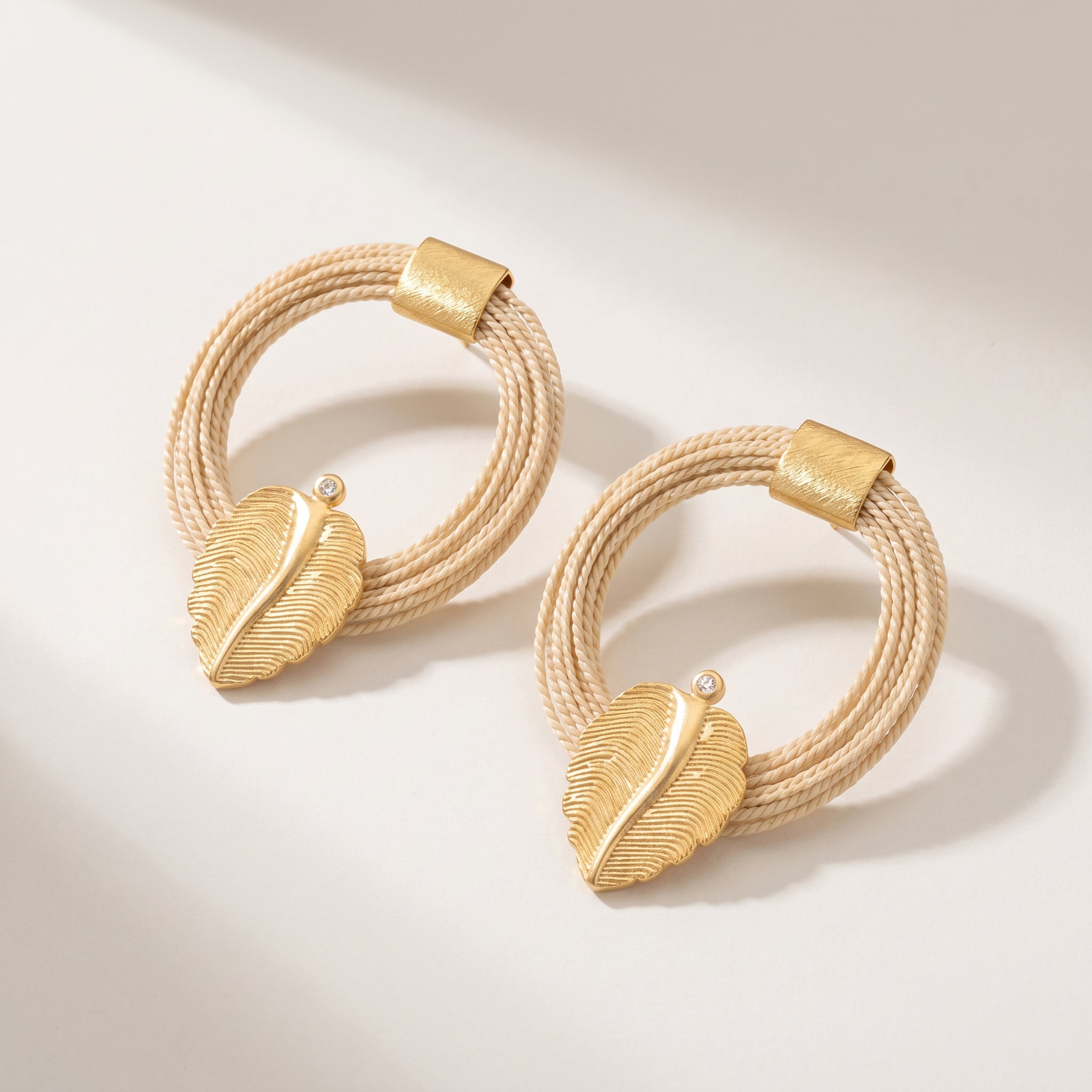 Purplee Store Buriti Artisanal Zariel Earrings Pair of gold hoop earrings with feather designs on a light background