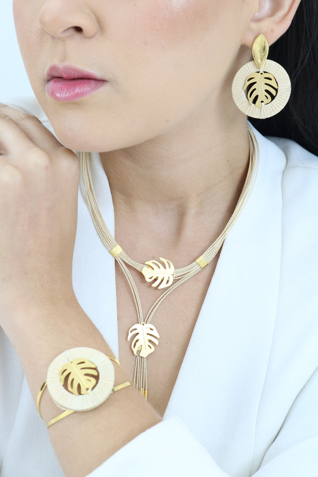 Mujer usando Conjunto de pendientes y pulsera y collar de Purplêe Store hechos a mano en palha de burití con diseño de hoja tropical dorada – joyas sostenibles inspiradas en la naturaleza