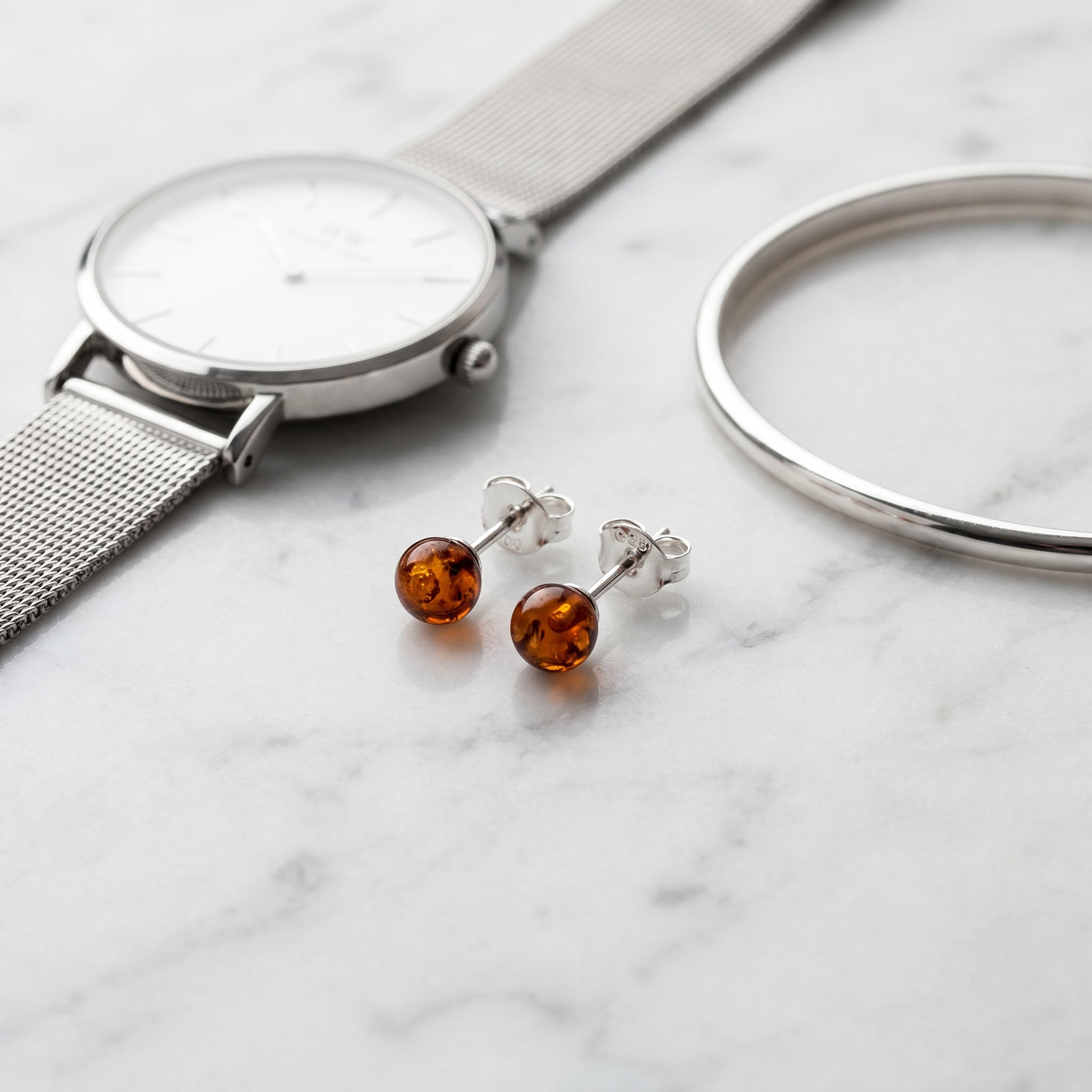 Silver watch, silver ring, and Amber Glow Cognac 925 Silver Studs|Purplee Store on a marble surface