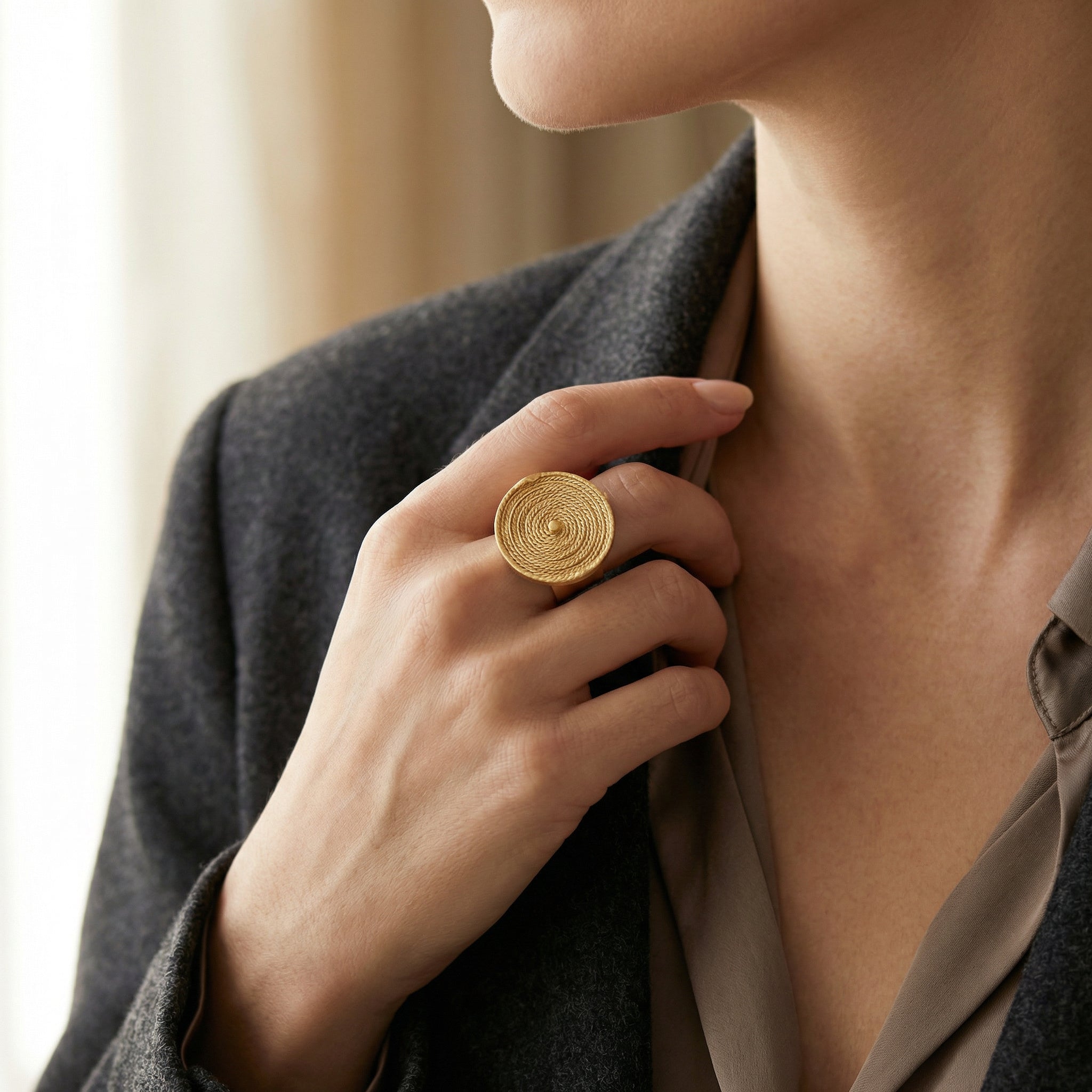Close-up of a woman wearing a Adjustable Buriti Ring, 18k Gold - Artisan Eco-Chic, holding a gray garment. Purplee Store