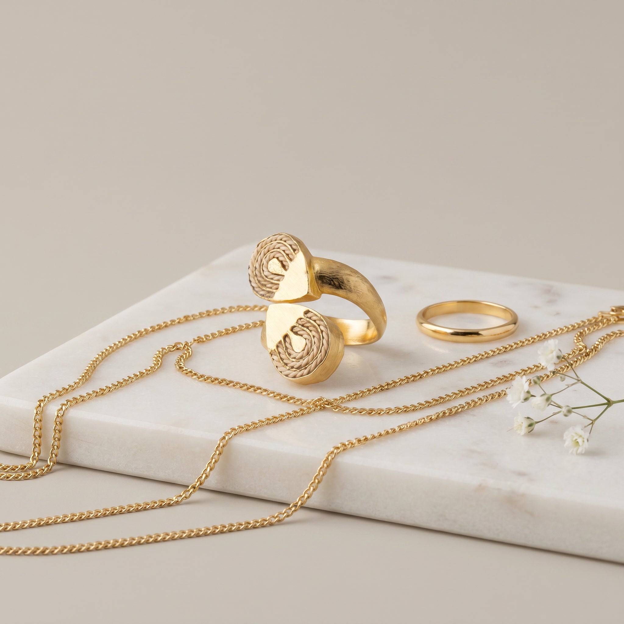 Gold jewelry including a necklace and two rings on a light surface with a neutral background. Purplee Store