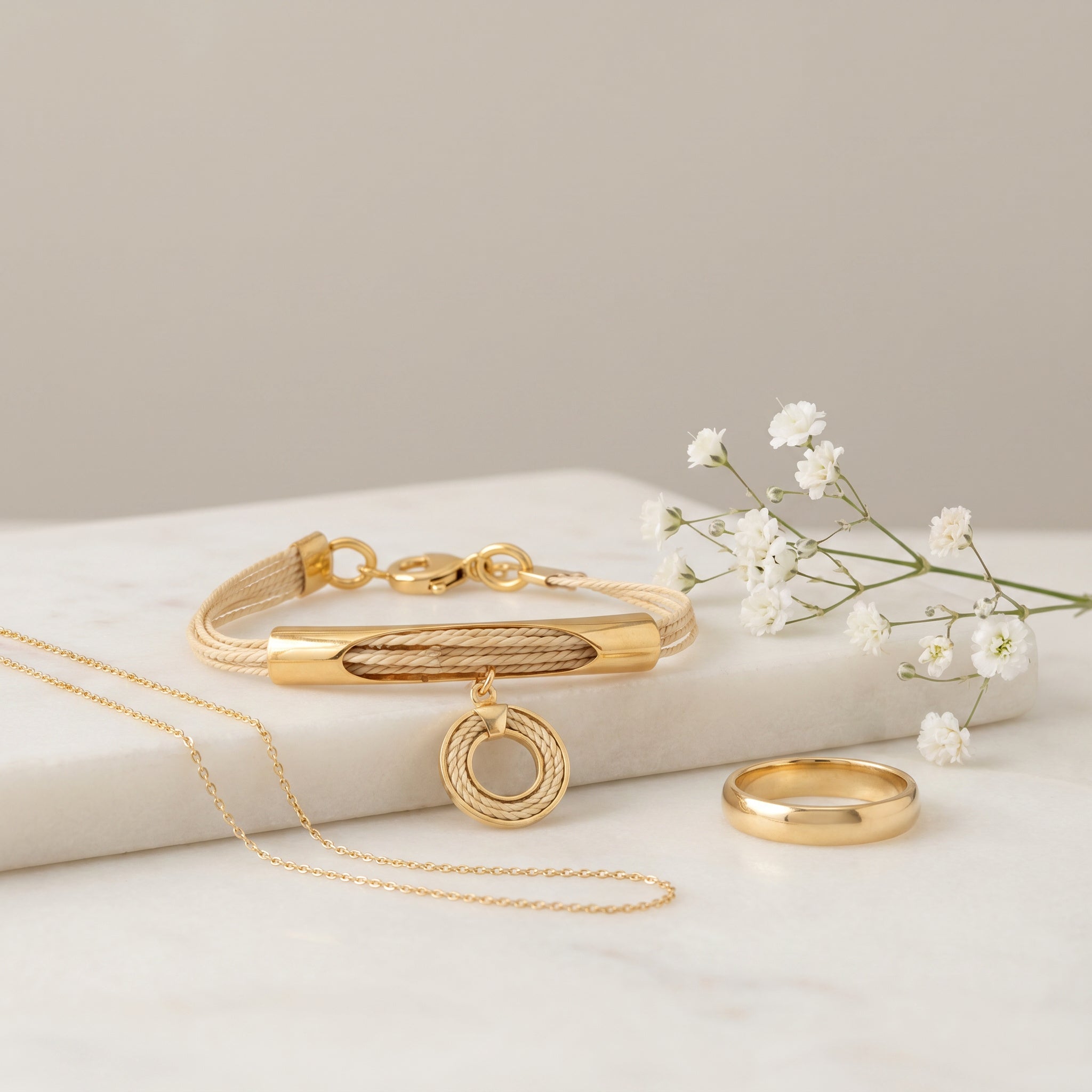 Gold jewelry set including a bracelet, necklace, and ring on a light background with small white flowers. Purplee Store