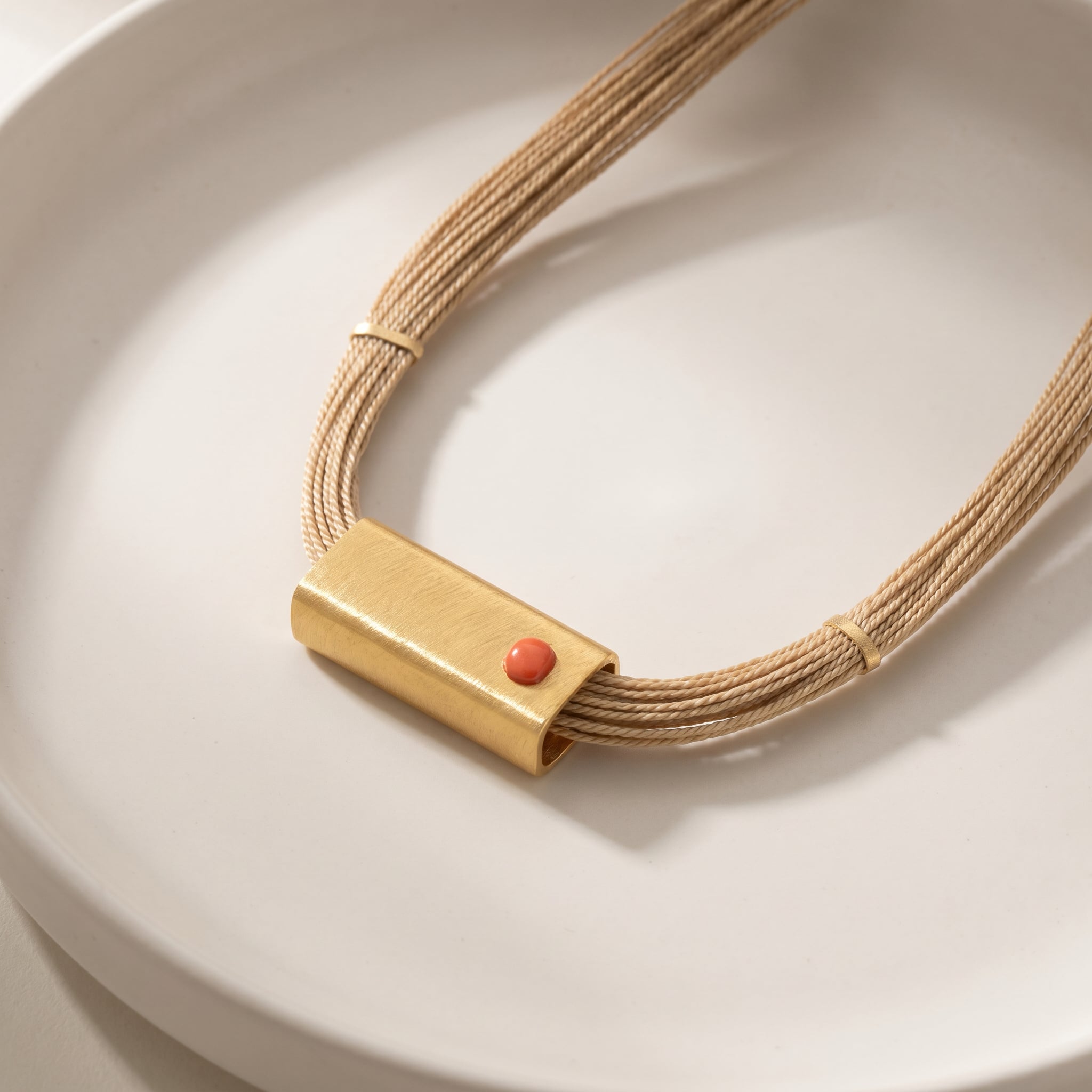 Purplee Store Buriti Geometric Orvellia Necklace with a gold clasp and red stone on a white plate