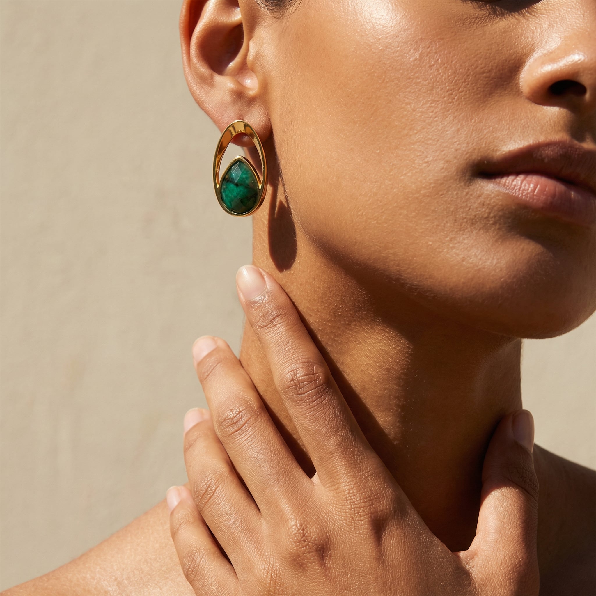 Close-up of a woman wearing a 24k gold plated earring with a genuine Emerald gemstone on a neutral background. | Purplee Store
