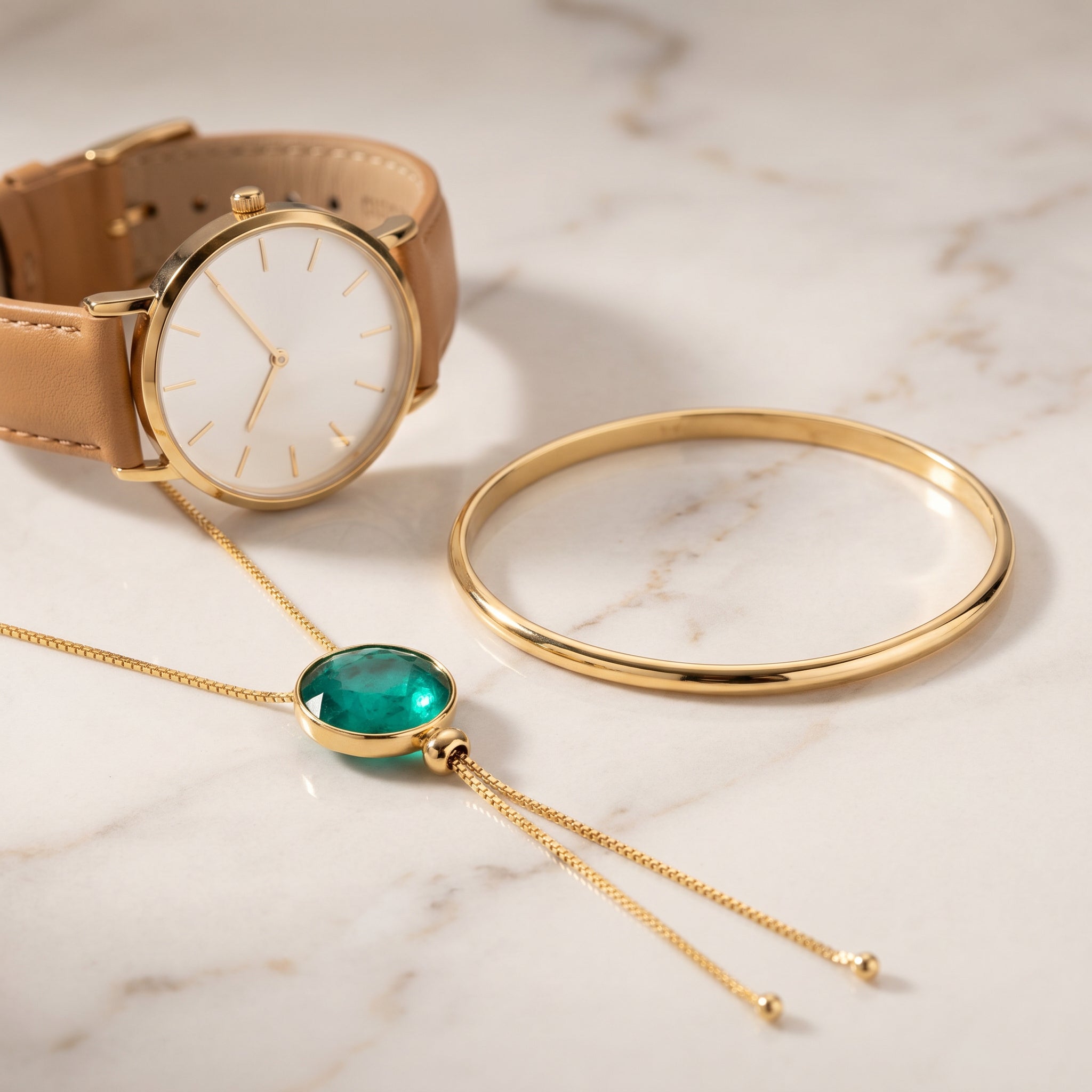 Gold watch, bangle, and Purplee Store ELAN Emerald Statement Necklace on a marble surface