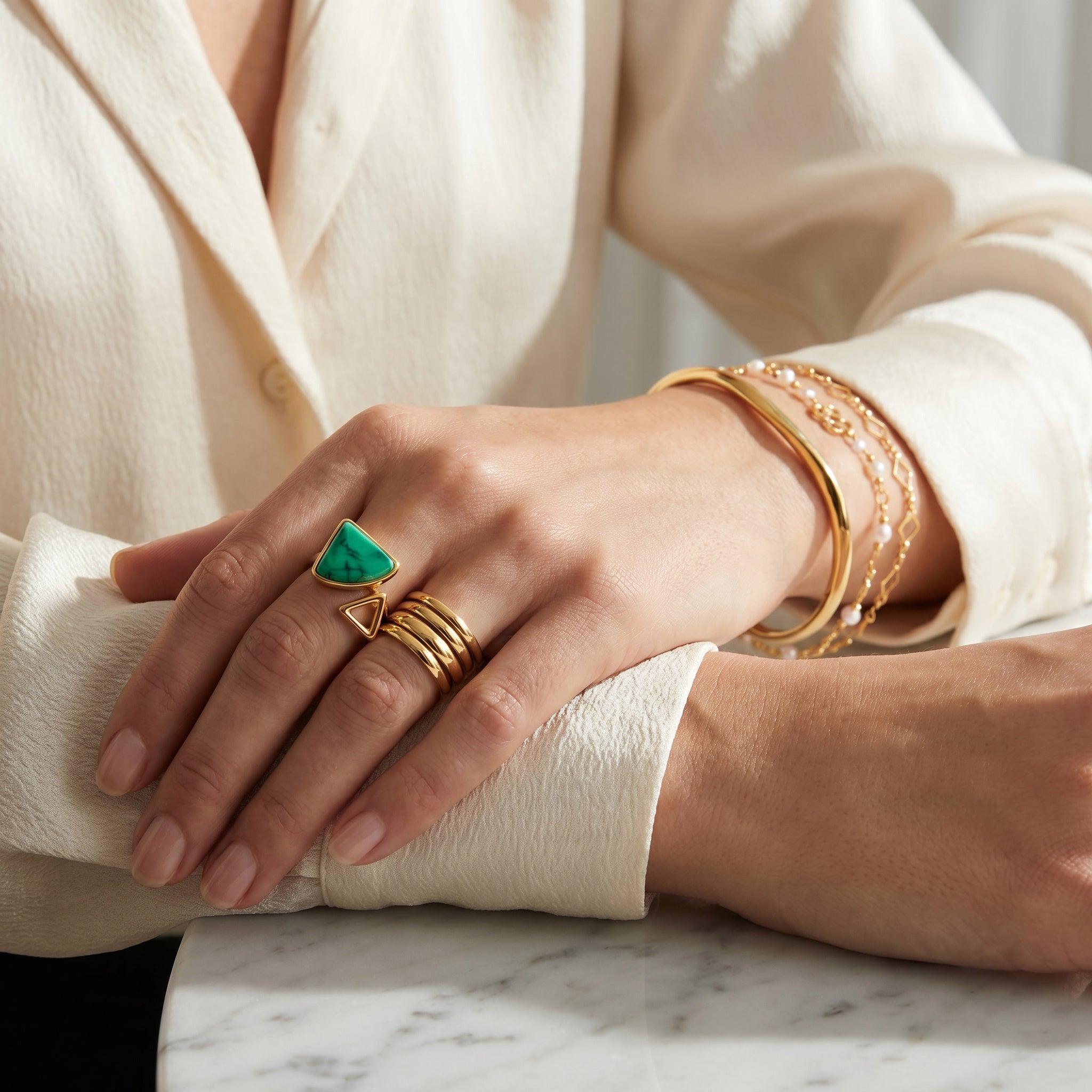 Hand wearing Purplee Store ELAN Geometric Bypass Ring and bracelets on a marble surface