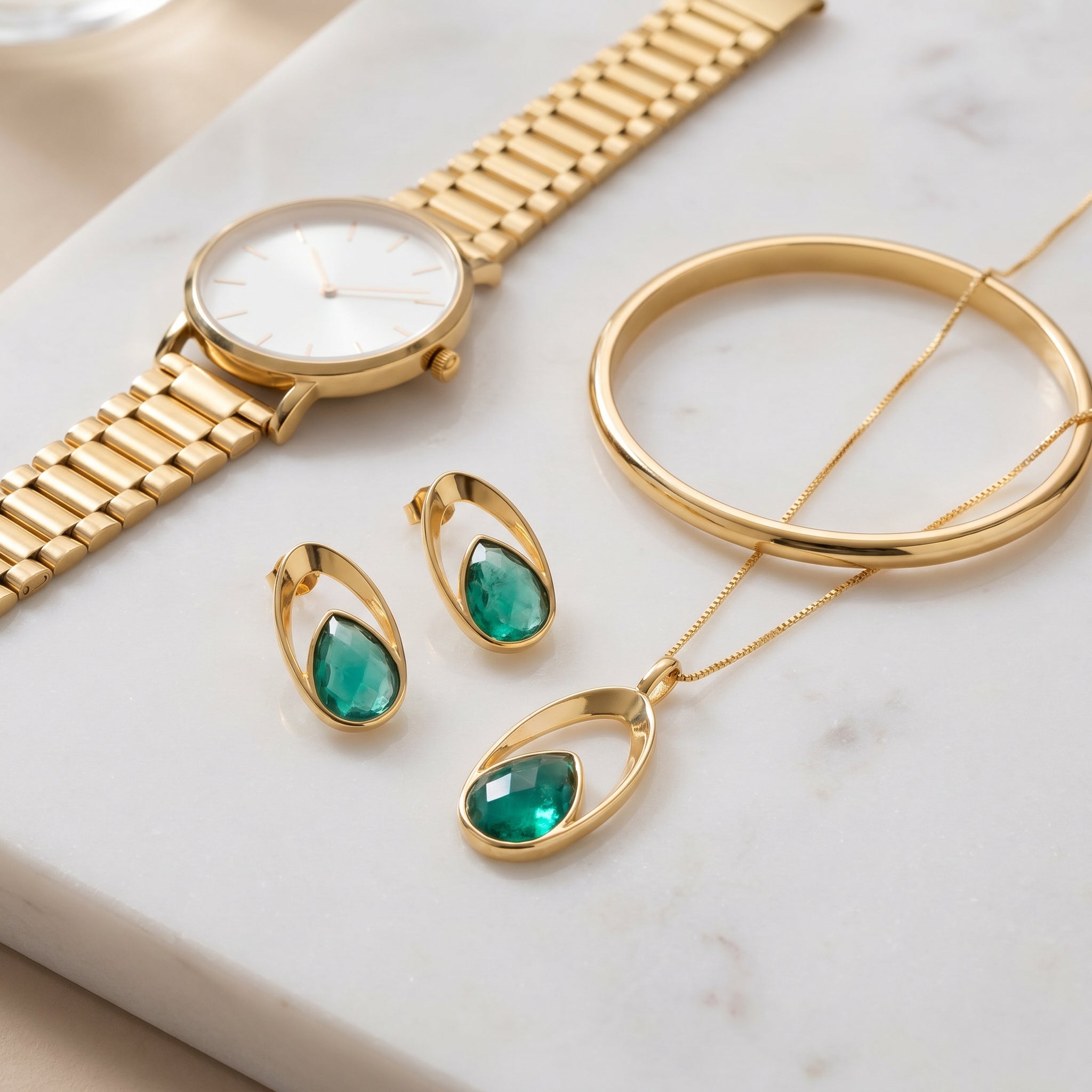 Purplee Store Gold watch, bracelet, and Emerald Orbit  set with emerald green stones on a marble surface