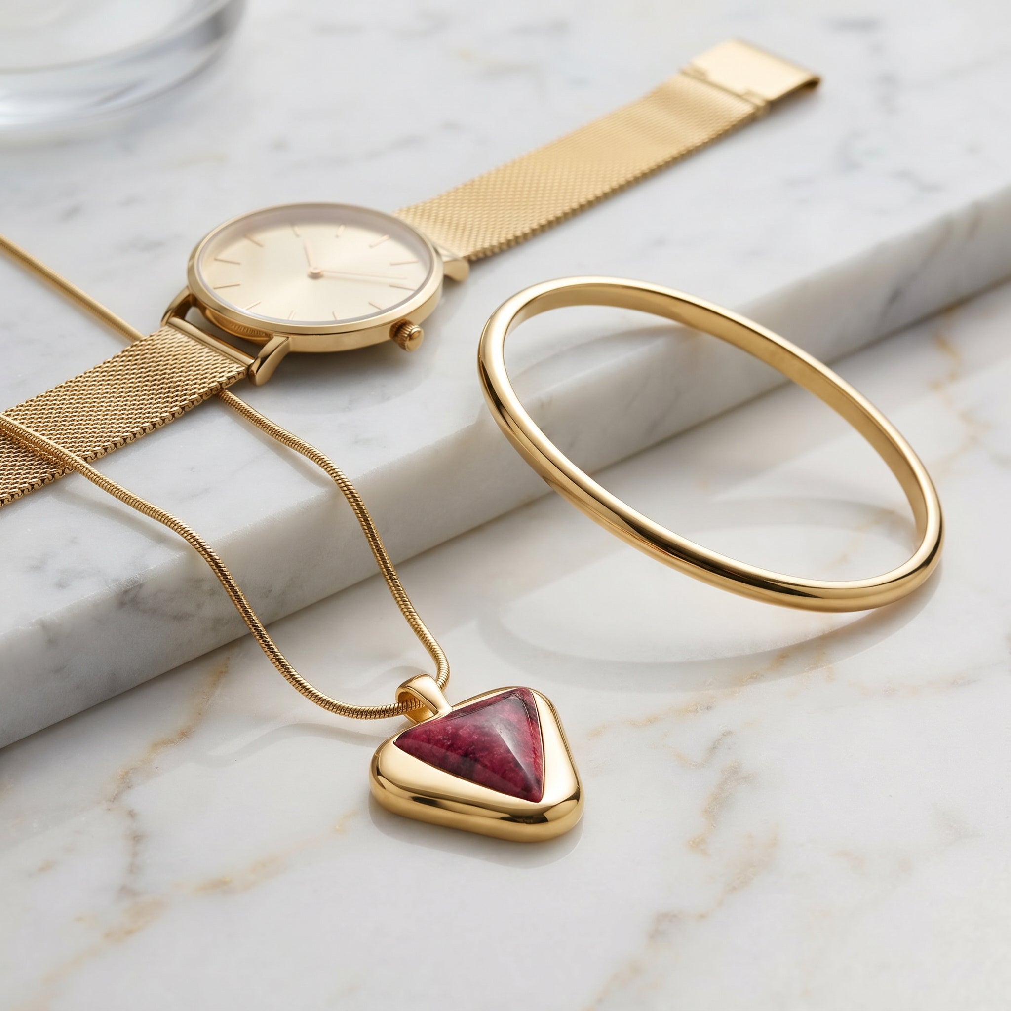 Gold watch, Purplee Store ICON Eclipse Luxury Rhodonite Pendant Necklacet, and gold bangle on a marble surface