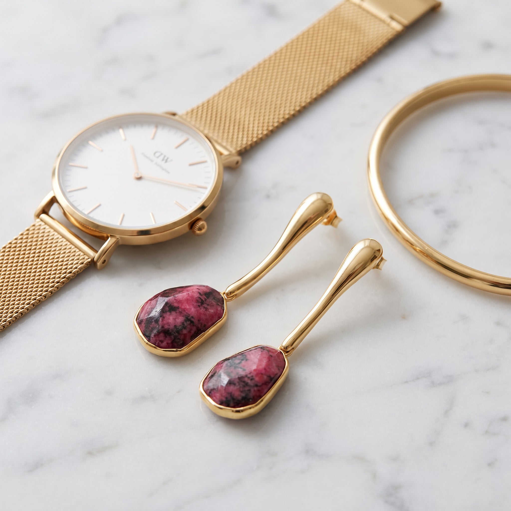 Gold watch, Purplee Store ICON Rhodonite Sculptural Earrings, and gold bracelet on a marble surface