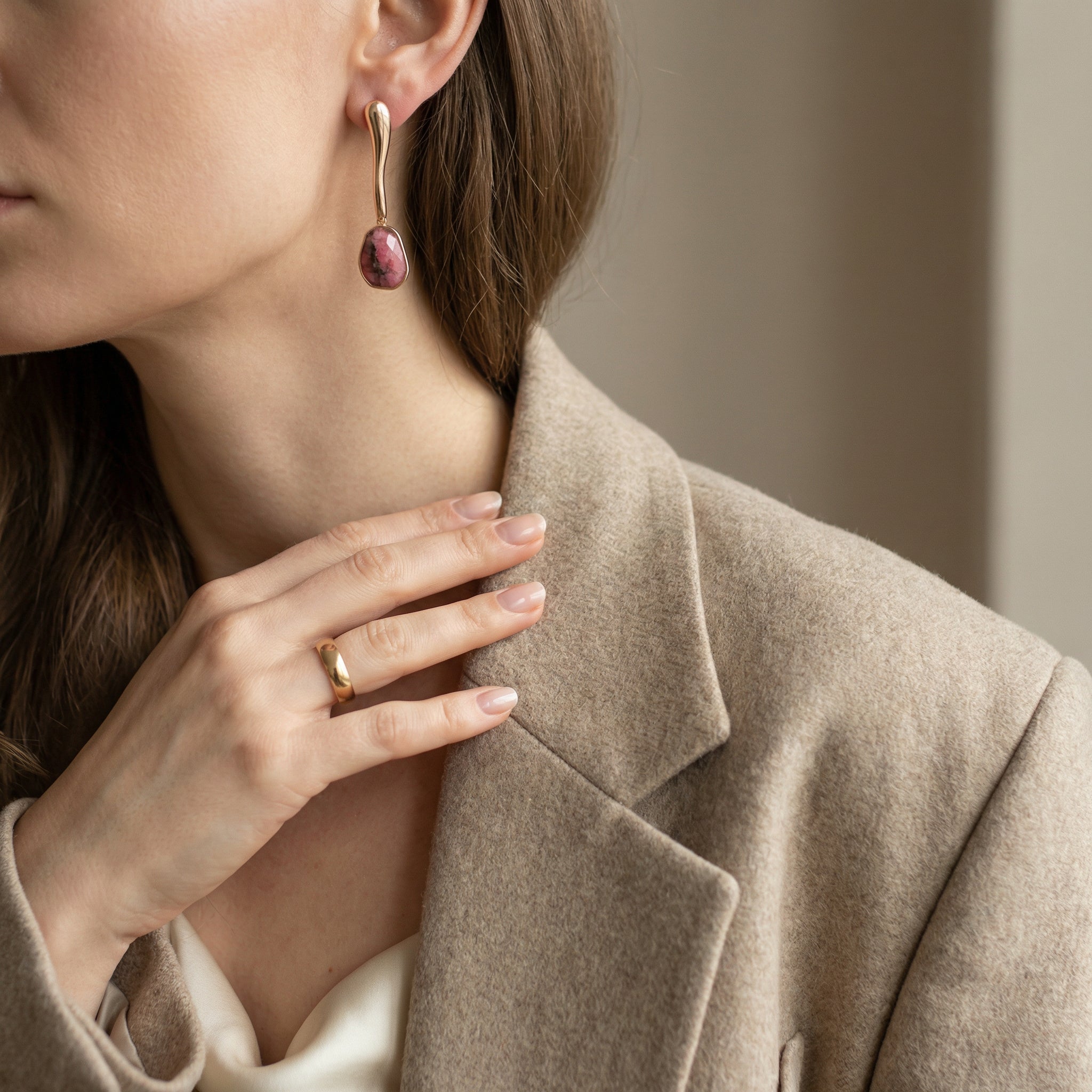 Close-up of a person wearing a gold earring 24k Gold & Rhodonite and ring, with a neutral background. Purplee Store