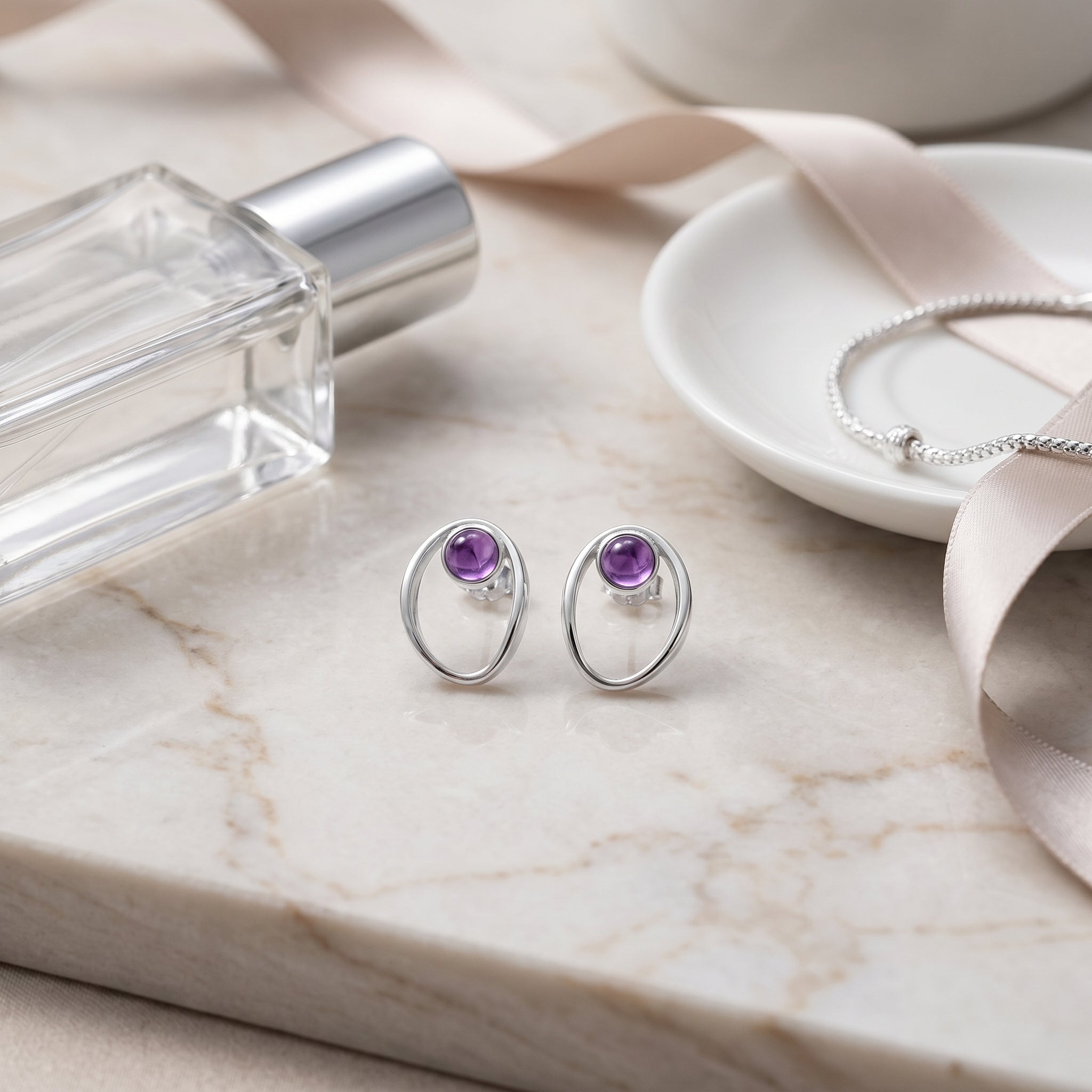 Purplee Store PIORELLE Sculpted Amethyst Earrings on a marble surface with a perfume bottle and jewelry box.