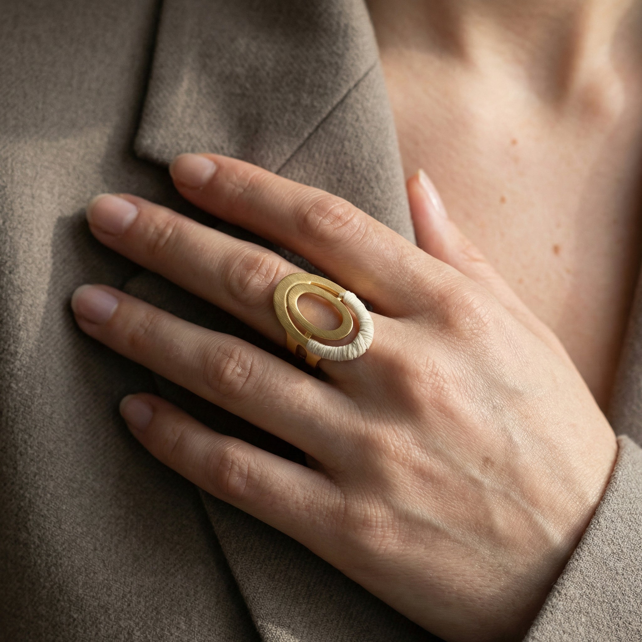 Hand wearing a Unique Buriti Sculptural Ring, 18k Gold Accents with a beige coat background. Purplee Store