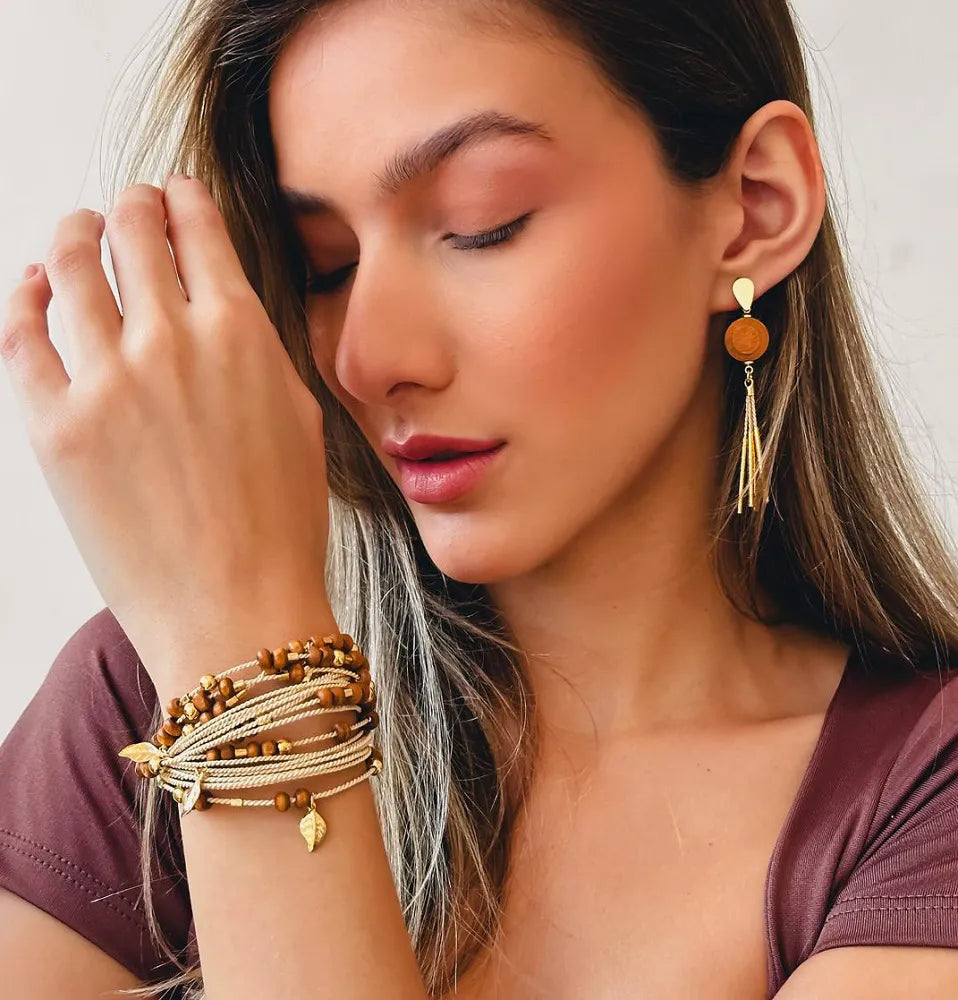 Mujer usando Conjunto de Purplêe Store con pendientes largos y pulsera hecha a mano en palha de burití, madera natural y detalles dorados – joyas sostenibles con esencia tropical