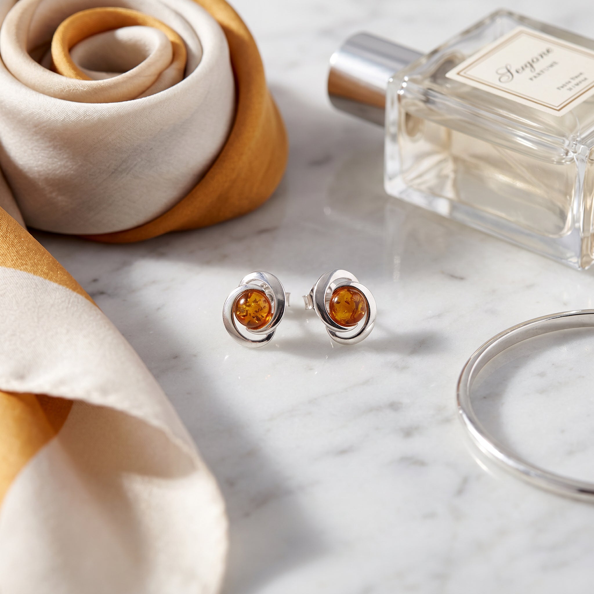 Amber Glow Round 925 Silver Drops|Purplee Store on a marble surface with a perfume bottle and fabric.